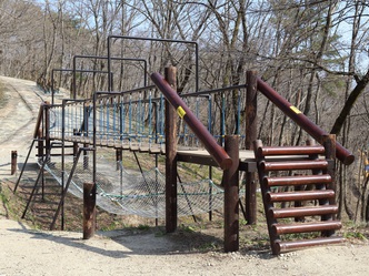 外で木製で作られた橋の遊具と遊具の下に網が設置されている写真