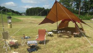 青空の下に芝生と木々が広がるキャンプ場の写真