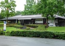 芝生や木々の間に佇む平屋建ての日本家屋の写真