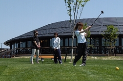 ゴルフヤードでスイングしている男性とそれを見守る女性たちの写真