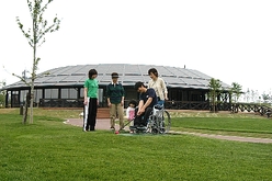 車椅子のプレーヤーがゴルフクラブをかまえているのを見守る人々の写真