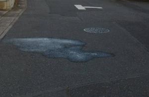 黒いアスファルト道路のマンホール付近で水が路上ににじみ出ている様子の写真