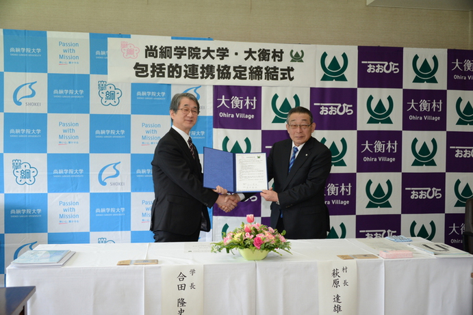 尚絅学院大学・大衡村包括的連携協定締結式と書かれた幕の前で締結所を持つ二人の男性の写真