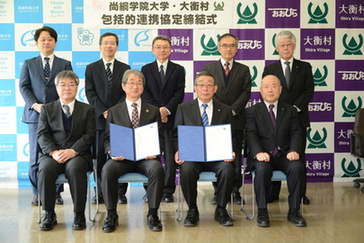 尚絅学院大学と大衡村のマークが書かれた壁の前に2列になって写真に写る9人の男性の写真