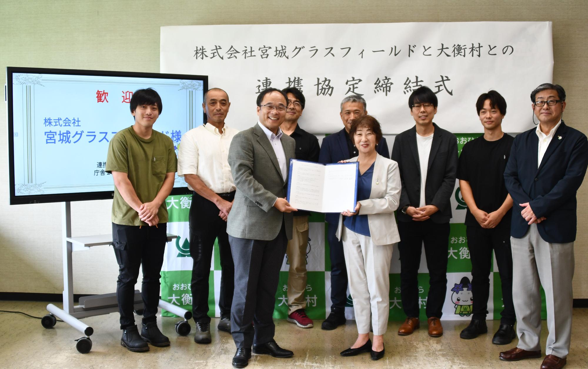 グラスフィールドとの連携協定締結式で参加者全員の集合写真。8人の男性と1人の女性が写っている。