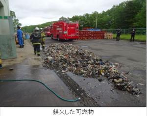 鎮火した可燃物の写真。奥には消防車が停まっている。