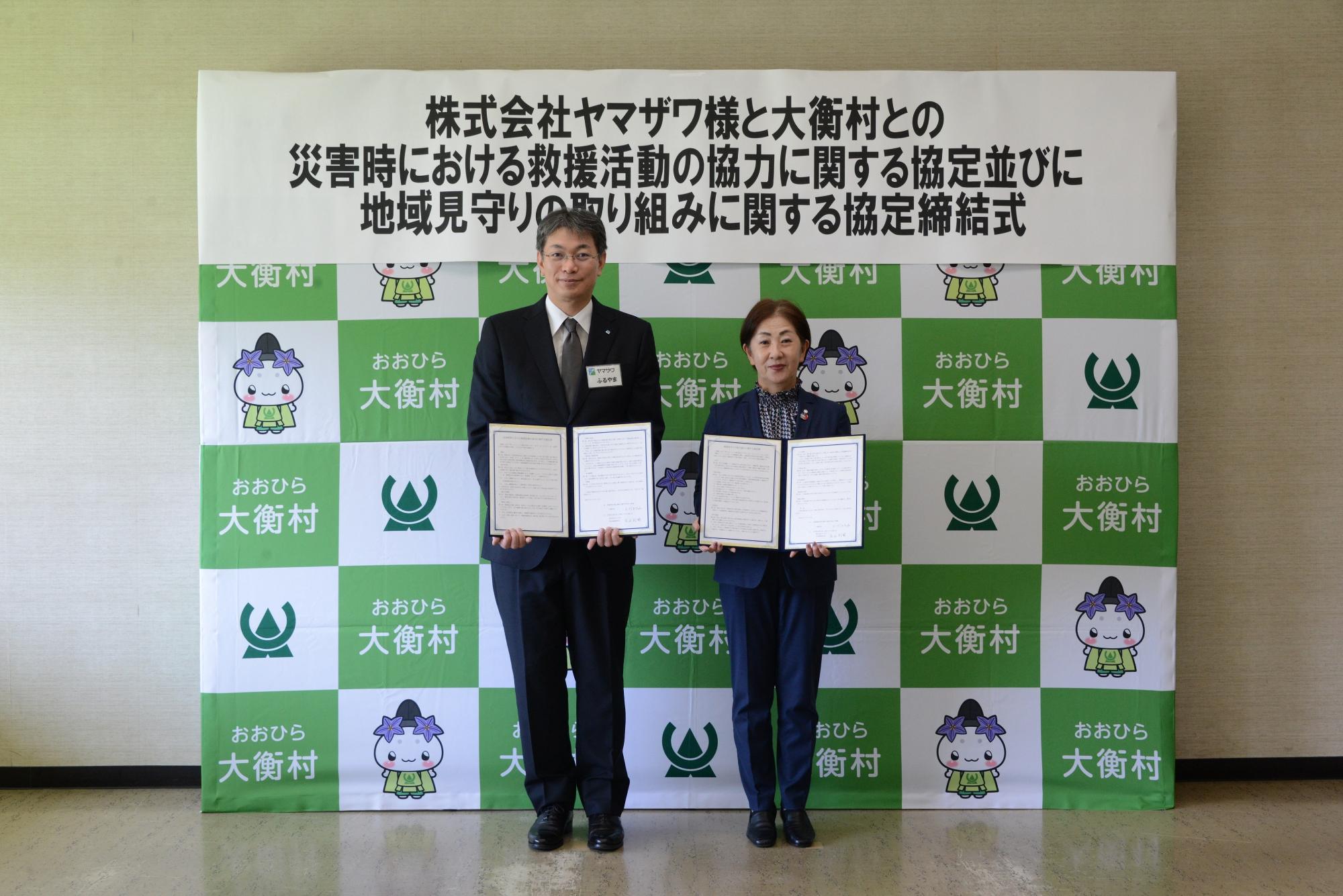 2つの協定を締結した株式会社ヤマザワ古山社長と大衡村長が並んで立って協定書を胸の前で広げている写真